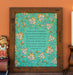 The "My Hope Is Built" hymn art print features a verse from the hymn surrounded by a delicate multicolored floral illustration against an aquamarine background, will compliment any room; shown here framed and styled with books, a ceramic figure, and a candle.