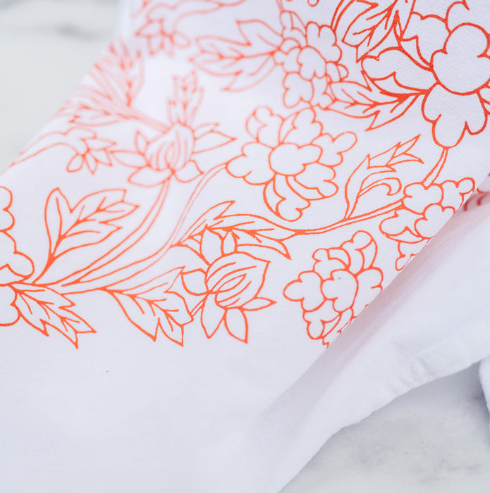 Little Things Studio presents the Nadine floral tea towel—100% cotton, made in the USA, with subtle florals in a cheerful coral, shown folded and up close so that illustration detail is clearly seen.