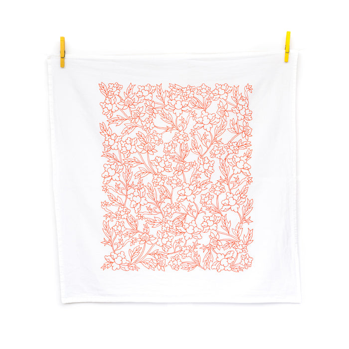 Little Things Studio presents the Nadine floral tea towel—100% cotton, made in the USA, with subtle florals in a cheerful coral, shown unfolded and hanging with clothes pins.