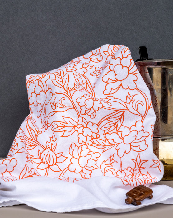 Little Things Studio presents the Nadine floral tea towel—100% cotton, made in the USA, with subtle florals in a cheerful coral, shown styled with a coffee carafe.