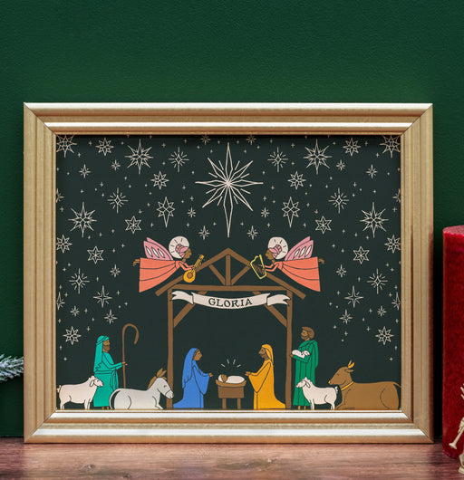 The Nativity Christmas art print features a vibrantly illustrated nativity scene surrounded by a striking night sky full of stars; shown in a gold frame accented by a candle