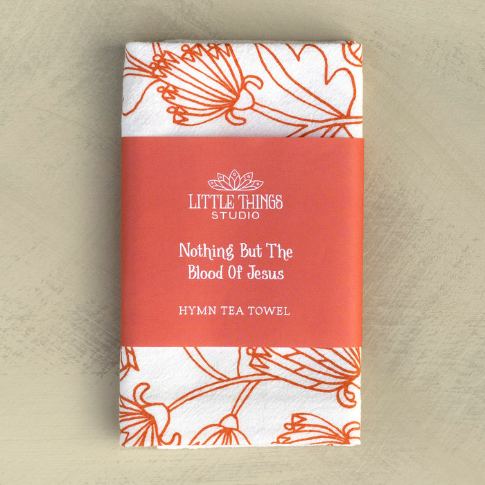 The Nothing But the Blood hymn tea towel is printed in sunset orange and features lyrics from the hymn accented by intricate floral illustration, shown folded and wrapped with a paper belly band for gift giving.