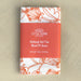 The Nothing But the Blood hymn tea towel is printed in sunset orange and features lyrics from the hymn accented by intricate floral illustration, shown folded and wrapped with a paper belly band for gift giving.