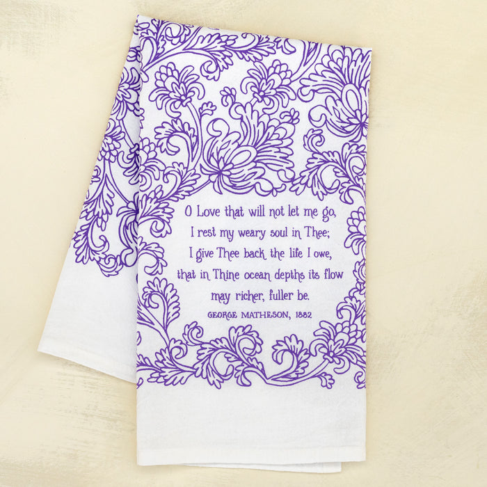 The "O Love That Wilt Not Let Me Go" hymn tea towel is printed in lavender and features floral illustrations and lyrics from the hymn. 100% cotton; US made, and shown here folded against a khaki background