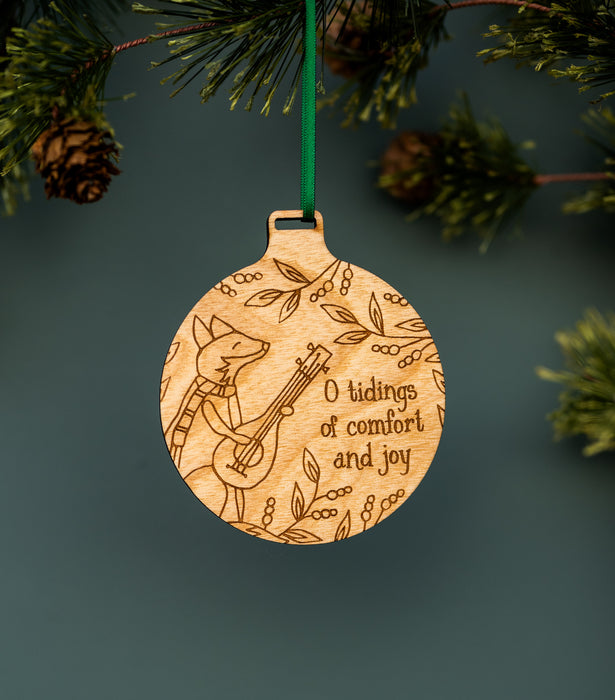 These bundled-up, ukulele-playing foxes—one of the new wood Christmas hymn ornaments from Little Things Studio — will add a touch of whimsy and cheer. Shown hung with ribbon from a Christmas tree.