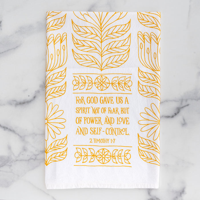 The Power, Love & Self-Control Scripture tea towel is printed in sunflower yellow and features 2 Timothy 1:7; shown folded against a gray marble background.