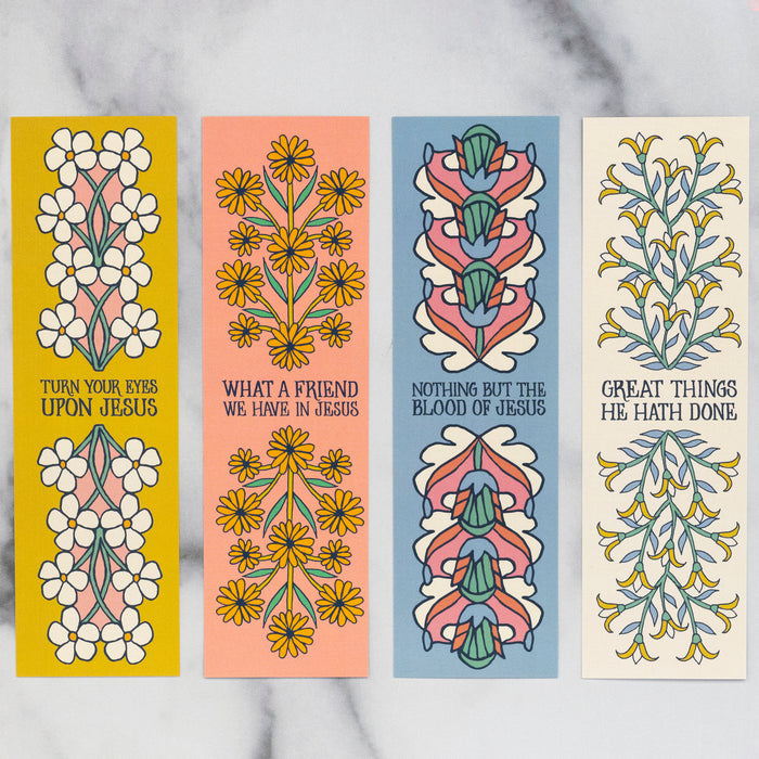 Lovely hymn bookmarks which feature phrases from beloved hymns adorned with vibrant florals on one side and complimentary floral patterns on the back; shown here in a row against a white marble background.