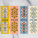 Lovely hymn bookmarks which feature phrases from beloved hymns adorned with vibrant florals on one side and complimentary floral patterns on the back; shown here in a row against a white marble background.