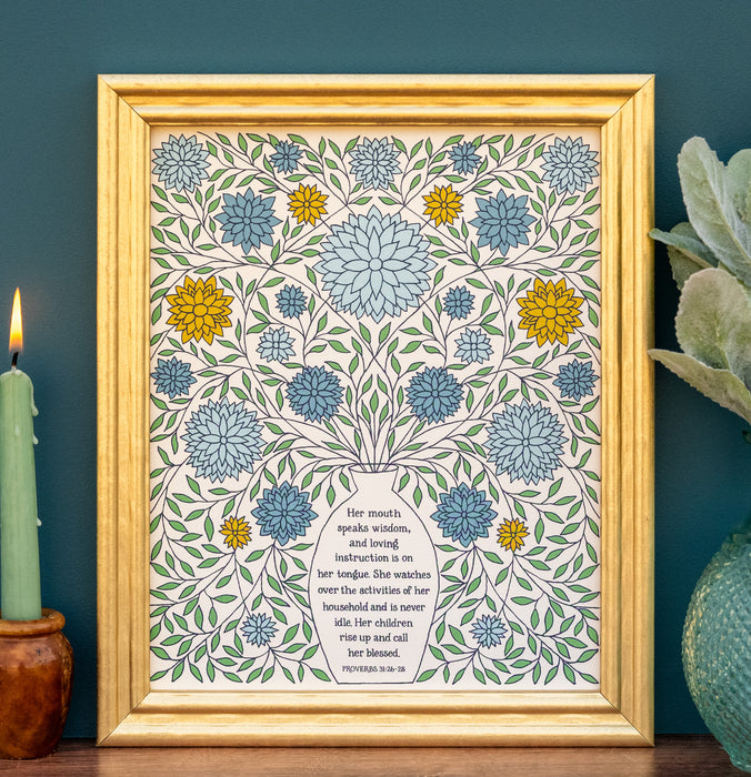 The "Rise Up and Call Her Blessed" art print features hand-lettered text from Proverbs 31 surrounded by delicate leaves and lush florals; shown in a frame and styled with a vase of greens and a candle.