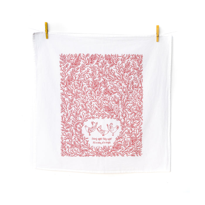 Our Silent Night Christmas hymn tea towel features a hand-illustrated floral border and hand-lettered text, printed in holly berry red on a 100% cotton tea towel, shown hanging with clothes pins.