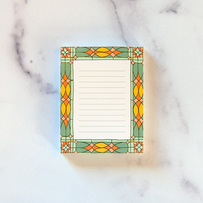 Small stained glass notepad with vibrant border illustration and lines for writing.