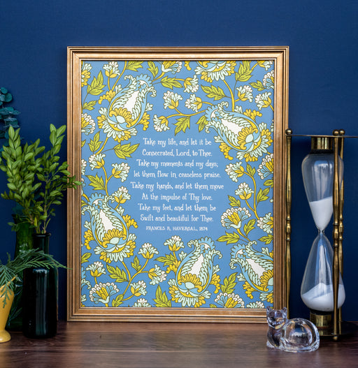 Take My Life, and Let It Be hymn art print features a bold green, gold, and aquamarine floral with a teal background, displayed in a copper colored frame, styled alongside fresh greens and an hourglass against a cobalt blue wall