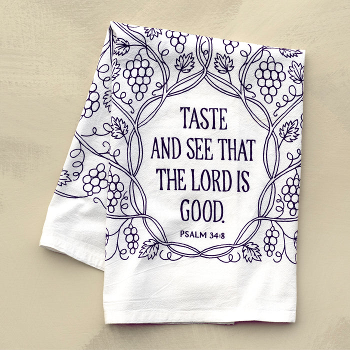 The Taste and See that the Lord Is Good Scripture tea towel is printed in concord purple and features Psalm 34:8; it is shown here folded against a khaki background.