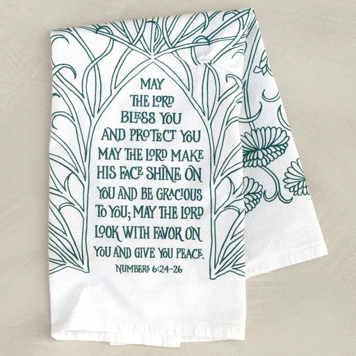 The Blessing Scripture tea towel is printed in muted blue-green tone and features the verse from Numbers 6:24–26. Made of 100% cotton. Shown here folded against a khaki background.