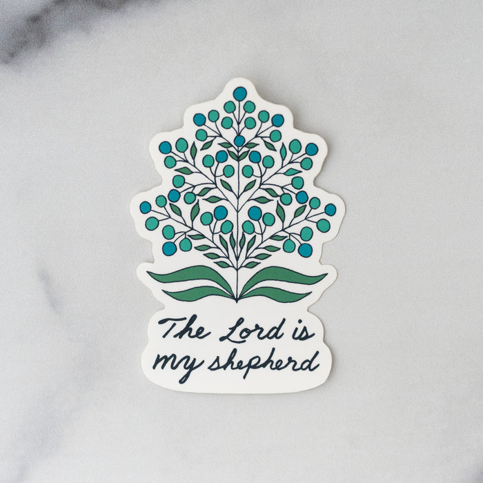 The “Lord is My Shepherd” sticker features hand-lettered text from Psalm 123 and reads "The Lord is my shepherd." The words are accented by a calming floral motif an eggshell background, shown against a gray marble background.