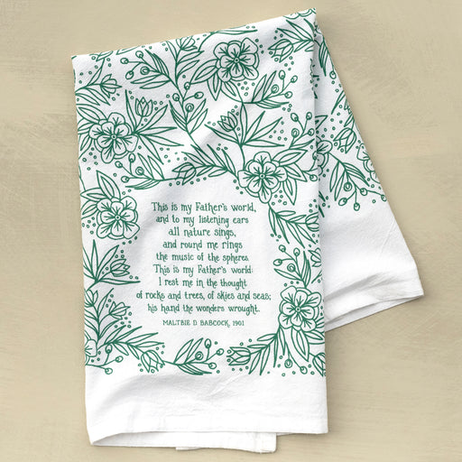 This is My Father's World tea towel is printed in teal and features hand lettered hymn text surrounded by intricate floral illustration, pictured folded against a khaki background