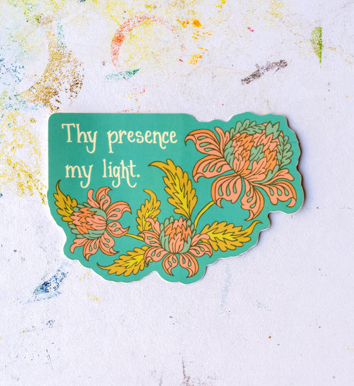 "Thy Presence My Light" hymn sticker has an aqua background with a coral and antique yellow motif and features lyrics from Be Thou My Vision. Shown against a worktable background.