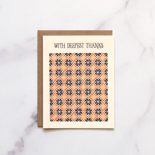 Our "With Deepest Thanks" Greeting Card is a hand illustrated geometric pattern highlighted with blues and corals on a pale yellow background, shown here against a marble background—a blank thank you card.