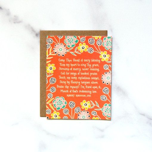 "Come Thou Fount" Greeting Card features a verse of the the loved hymn framed by a bold floral with an orange background, shown against a marble backdrop.
