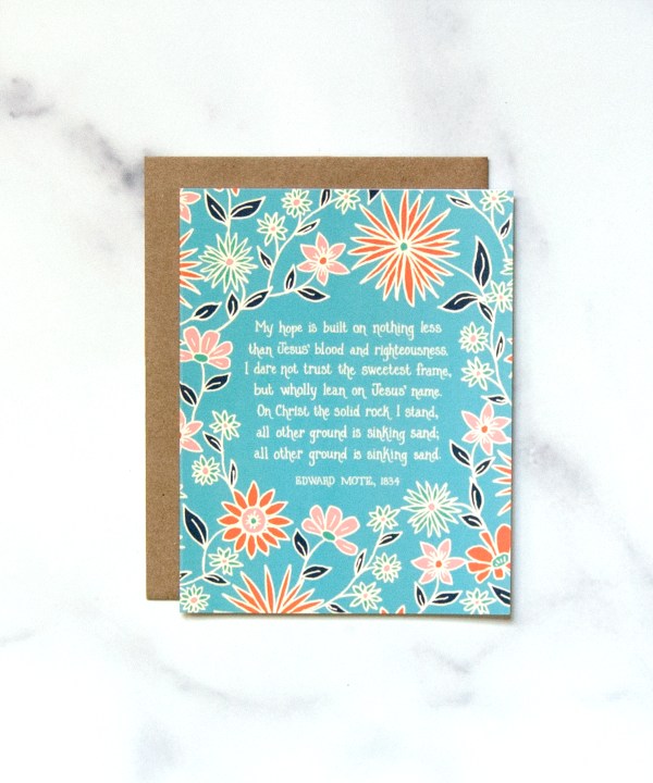 "My Hope Is Built on Nothing Less" Greeting Card features a verse of the cherished hymn framed by a lively floral in blues and corals, paired with a kraft paper envelope, shown against a marble backdrop.