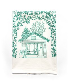 The winter tea towel is printed in pine needle green and features whimsical seasonal illustrations surrounding a winter cottage — could be used as a Christmas tea towel. Shown here folded against a white background.