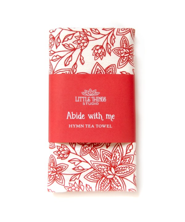 Abide with Me hymn tea towel printed in country red, folded and displayed with the printed paper belly band for gift giving