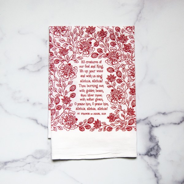 All Creatures of our God and King tea towel is printed in rich crimson, displayed folded against a white marble background