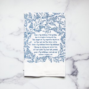 Great Is Thy Faithfulness tea towel is printed in a striking cobalt blue. The hand lettered text is surrounded by illustrated floral design, and the towel is shown folded against a white marble background.