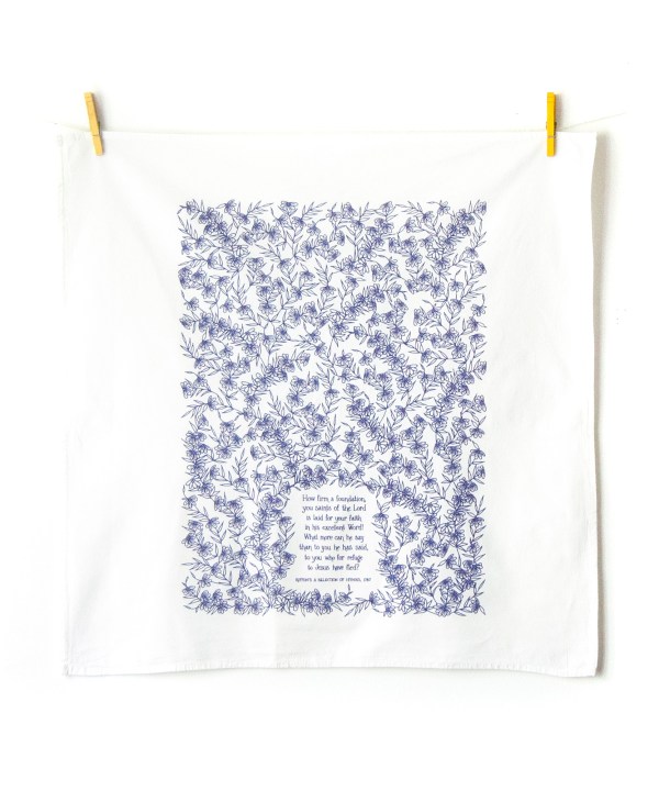 How Firm a Foundation hymn tea towel is printed in periwinkle and displayed unfolded, hanging with clothes pins