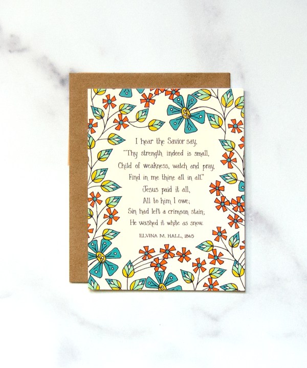The Jesus Paid It All greeting card features bright floral illustrations against a cream background, surrounding the first verse of the beloved hymn. Pictured against a white marble background.