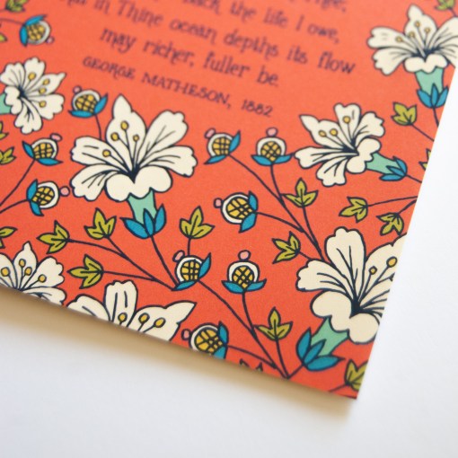 Floral and text detail of the "O Love That Will Not Let Me Go" greeting card, which features a striking white floral border framing the text with a deep red-orange background.