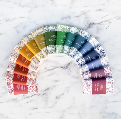 A hymn tea towel set of 16 Little Things Studio tea towels, displayed in the rainbow of colors against a marble backdrop