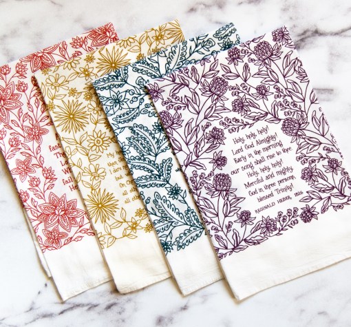 4 set of our hymn tea towels — lovely Christian kitchen towels — folded and lying on a white marble background.