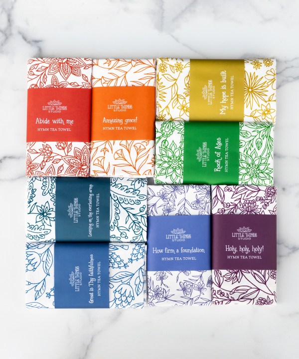 Set of 8 hymn tea towels (set 2) all displayed folded and wrapped in belly bands for gift giving, pictured on a white marble background.