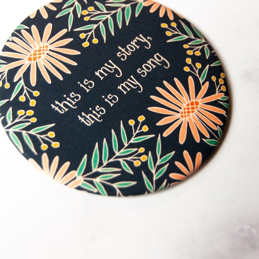 The "Blessed Assurance" hymn magnet, featuring the lines from the hymn, "this is my story, this is my song" surrounded by bright floral with a navy blue background, shown against a marble backdrop.