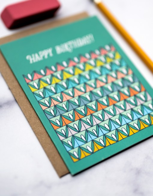 happy birthday greeting card with green background and colorful repeating pattern on a table with a pencil and eraser
