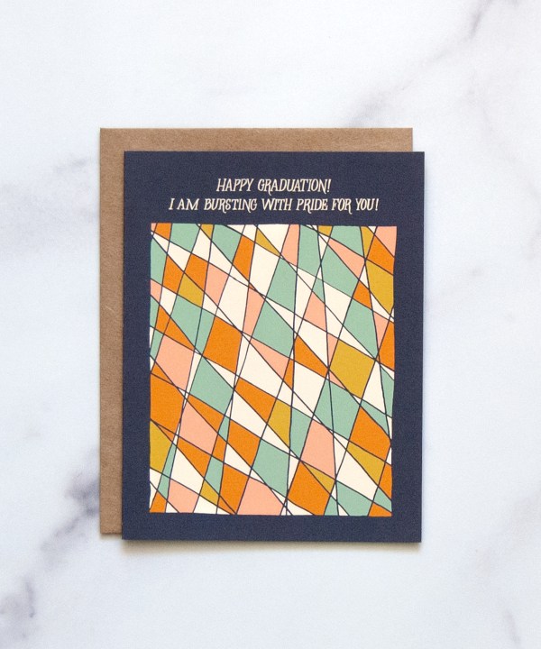 The graduation greeting card features abstract stained glass design that shines against a navy background, shown here against a white marble background.