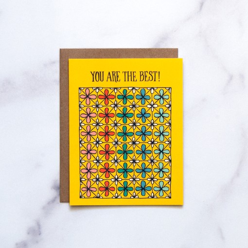 The "You Are the Best!" Greeting Card features hand illustrated patterned floral in an array of rainbow colors on a bright yellow background, shown here against a marble backdrop.