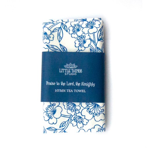 Praise to the Lord the Almighty hymn tea towel is printed in cobalt, displayed folded with a printed belly band for gift giving