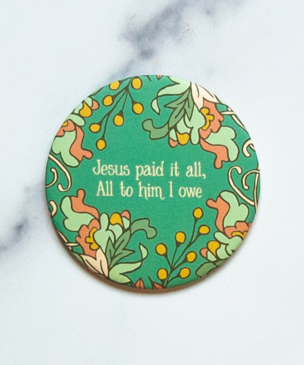 "Jesus Paid It All" hymn magnet features a phrase from the hymn in hand lettered hymn text surrounded by intricate floral over the teal background, shown against a marble backdrop.