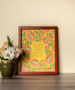 How Firm a Foundation art print — hand-lettered hymn text on a mustard background surrounded by a floral design using light red, light blue and green, pictured in a dark wood frame next to a vase of fresh flowers
