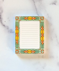 Small stained glass notepad with vibrant border illustration and lines for writing.