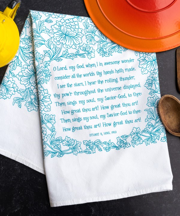 How great thou art tea towel in aqua blue sitting on a counter with baking dishes
