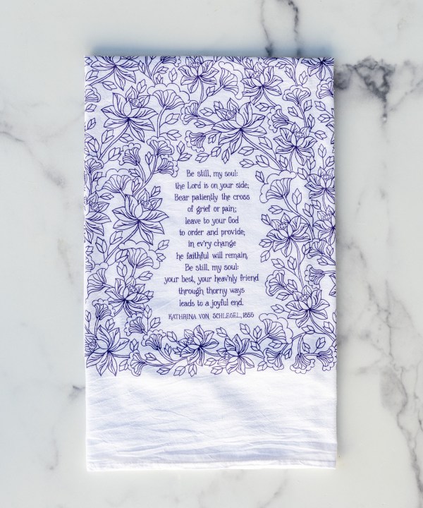 The Be Still, My Soul hymn tea towel featuring the beloved hymn is printed in a deep eggplant purple, shown folded against a marble background.