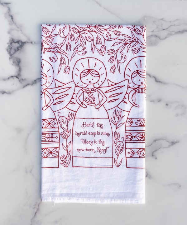 Hark! The Herald Angels Sing Christmas hymn tea towel features lyrics of two hymns: one for Advent ("The world in solemn stillness lay, to hear the angels sing" from It Came Upon a Midnight Clear) and one for Christmas ("Hark! The herald angels sing, 'Glory to the newborn King!'"). As usual, the tea towel features beautiful hand-lettered design with a floral border and our iconic heralding angels, printed in cranberry on a 100% cotton tea towel, shown folded on a marble background.