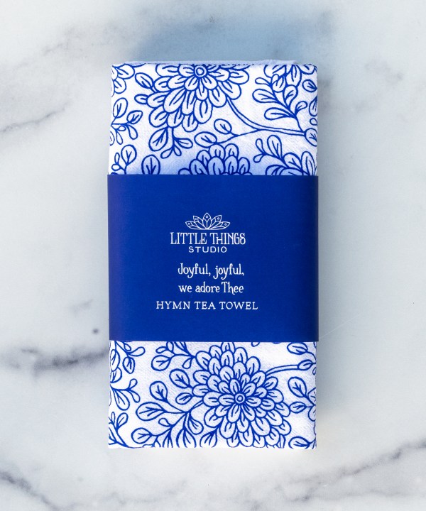 Joyful, Joyful We Adore Thee hymn tea towel features the beloved hymn is printed in blackberry blue, shown folded with a paper belly band for gift giving