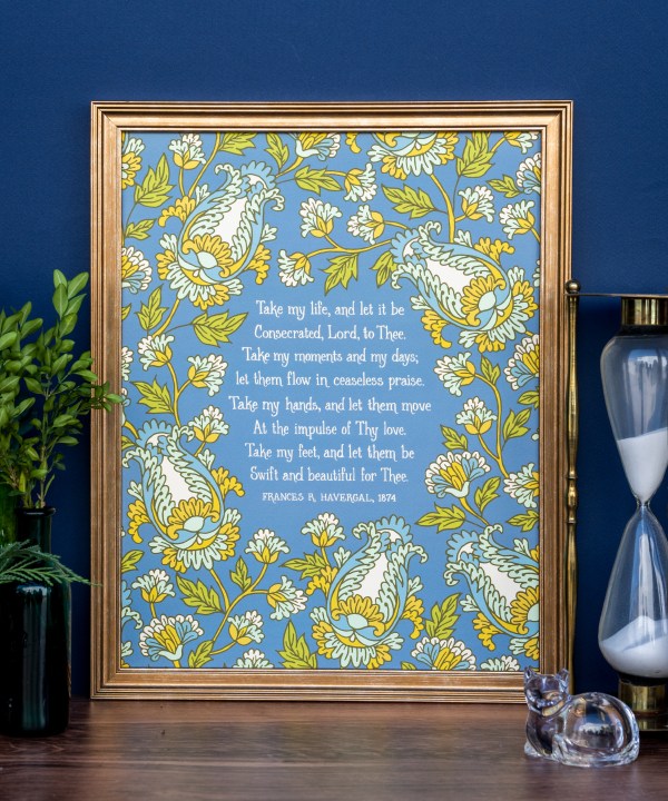 Take My Life, and Let It Be hymn art print features a bold green, gold, and aquamarine floral with a teal background, displayed in a copper colored frame, styled alongside fresh greens and an hourglass against a cobalt blue wall