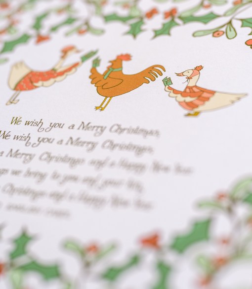 Illustration and text detail of We Wish You a Merry Christmas carol art print, which features illustration of lovely holly branches with festive animal carolers against a cream background