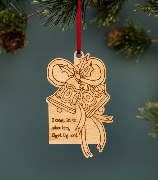These cheerful Christmas bells trimmed with ribbon and holly are one of the all new wooden Christmas hymn ornaments from Little Things Studio; shown hung with ribbon from a Christmas tree.