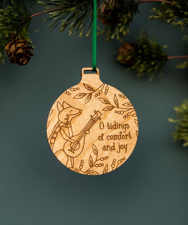 These bundled-up, ukulele-playing foxes—one of the new wood Christmas hymn ornaments from Little Things Studio — will add a touch of whimsy and cheer. Shown hung with ribbon from a Christmas tree.